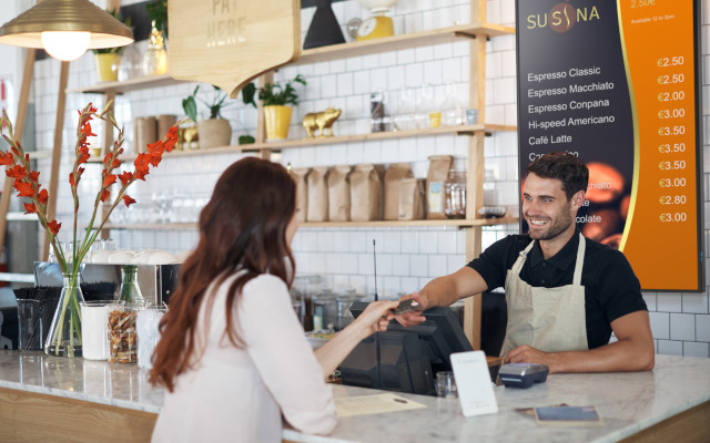 A man in an apron serves a woman over the counter in a coffee shop